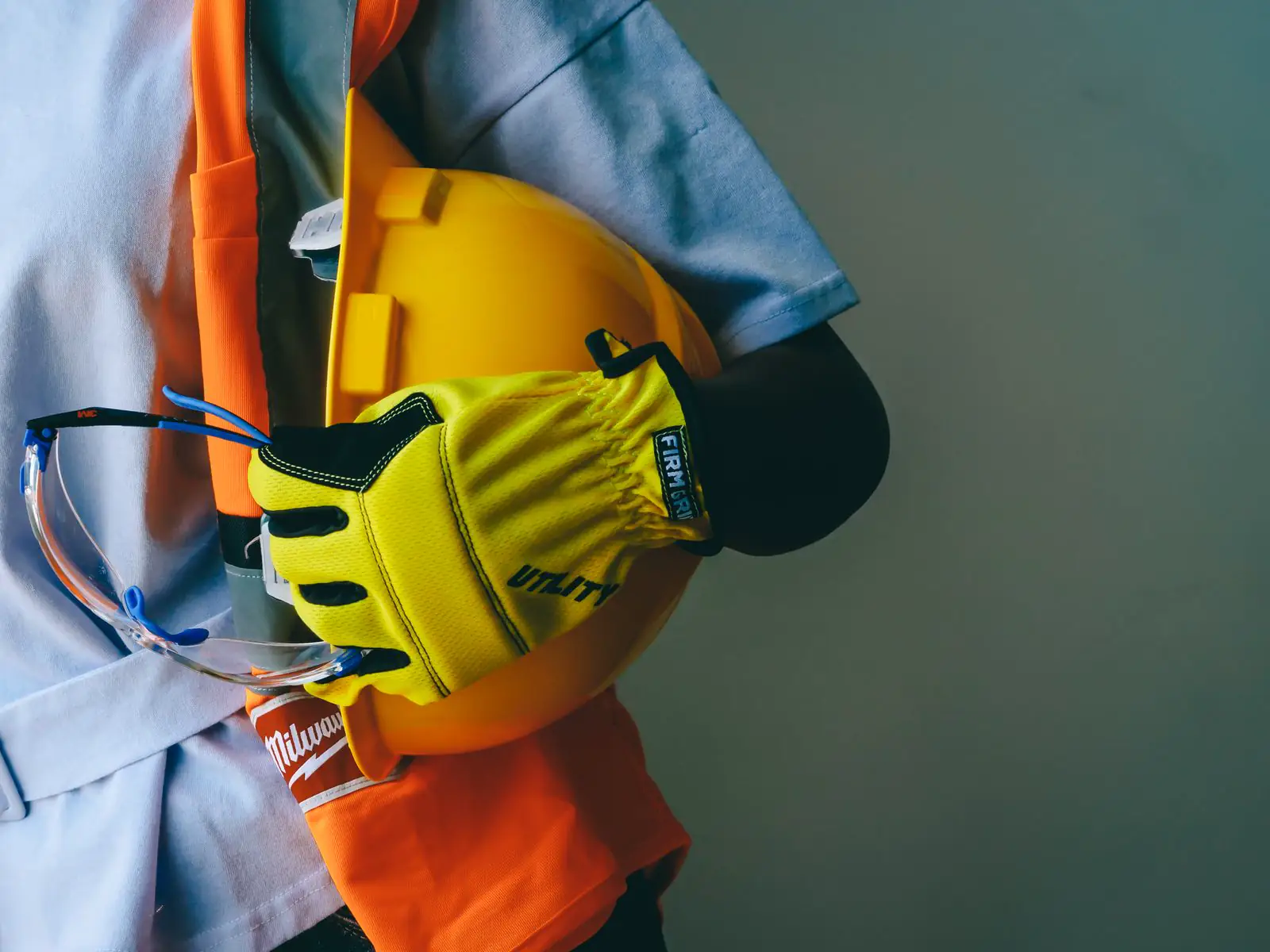 Casco amarillo, chaleco naranja y gafas de protección colgados de un arnés